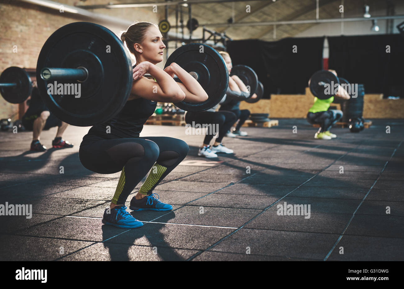 Fit young woman lifting des barres à l'accent, s'entraîner dans un gymnase avec d'autres personnes Banque D'Images