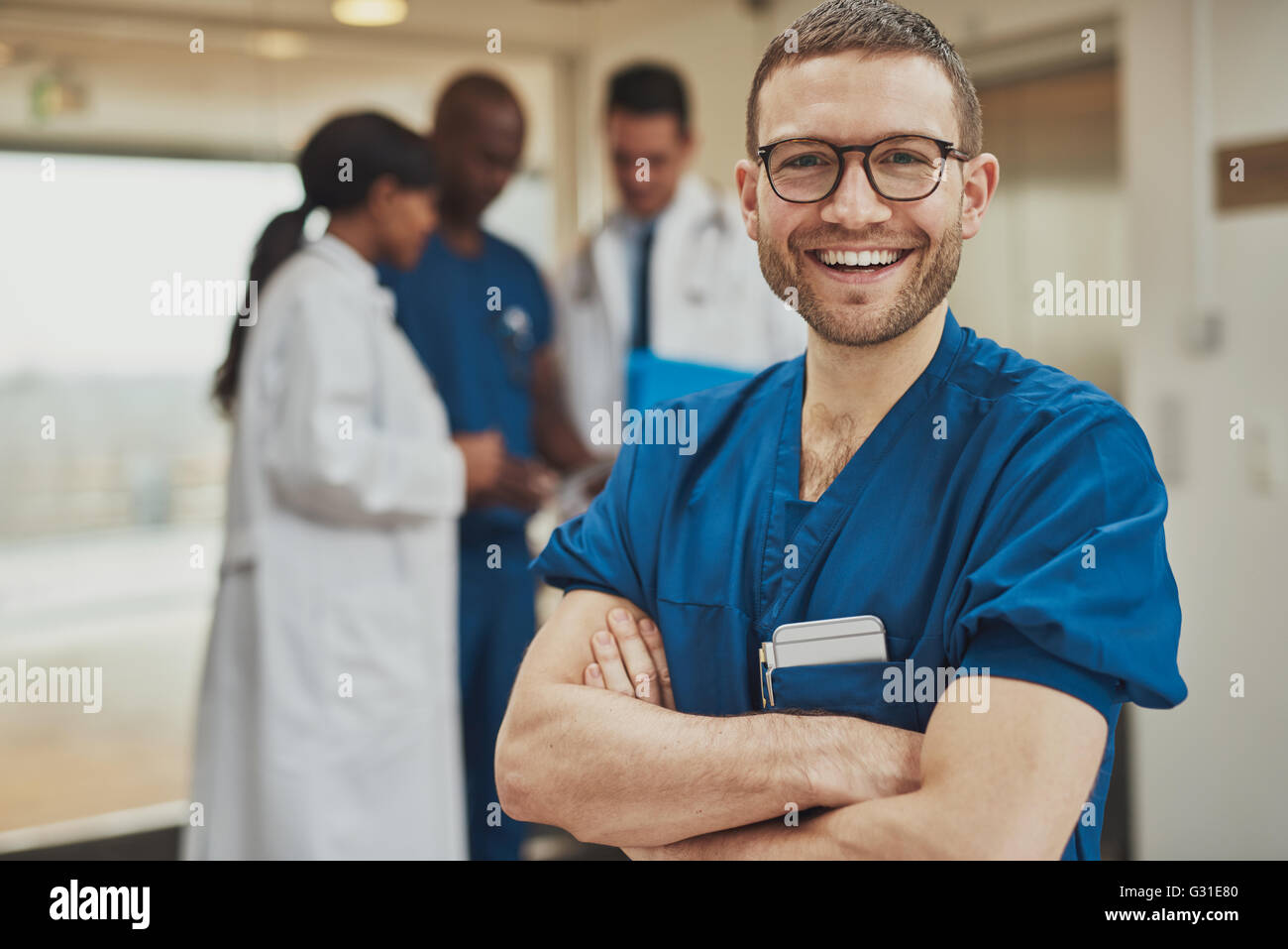 Jeune homme optimiste souriant chirurgien hôpital debout devant ses collègues de la transmission à l'appareil photo Banque D'Images