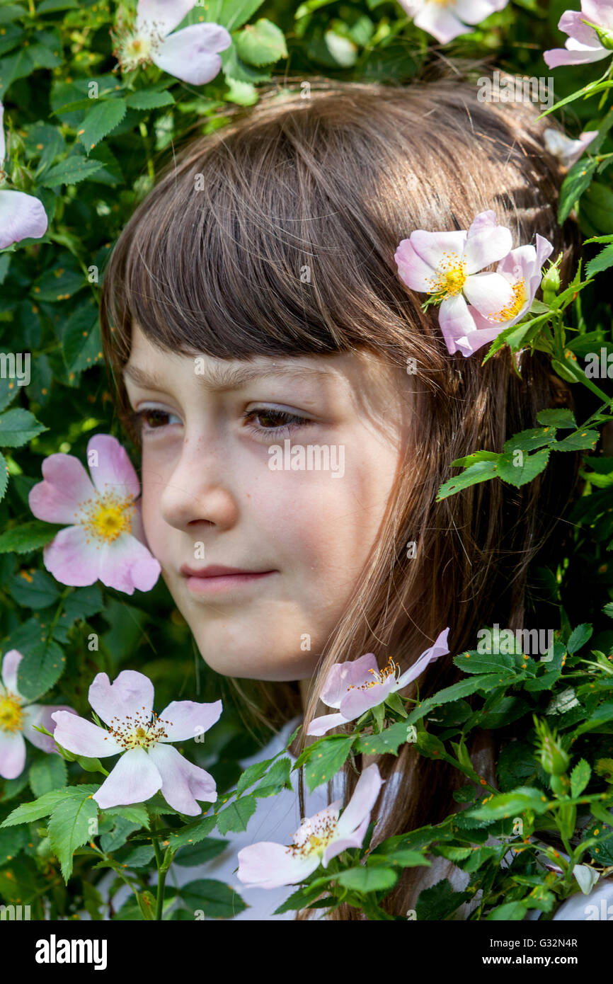 Fille de 7 ans enfant dans un arbuste fleuri de roses sauvages visage d'enfant portrait Banque D'Images