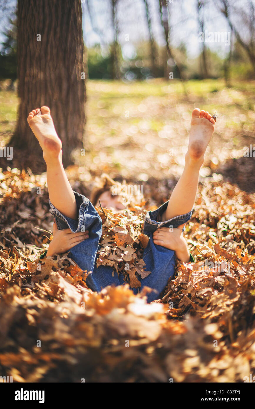 Garçon couché dans la pile de feuilles de l'automne avec les jambes en l'air Banque D'Images