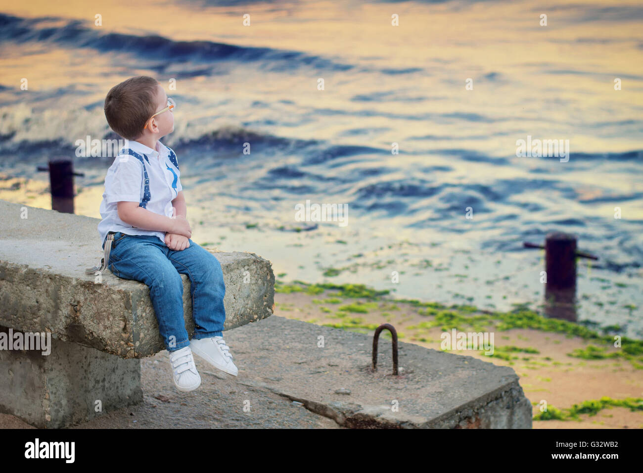 Garçon assis sur un banc au bord de la mer Banque D'Images