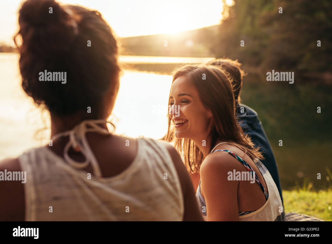Portrait of happy young woman sitting by a lake avec ses amis. Les jeunes passer une journée au bord du lac. Banque D'Images