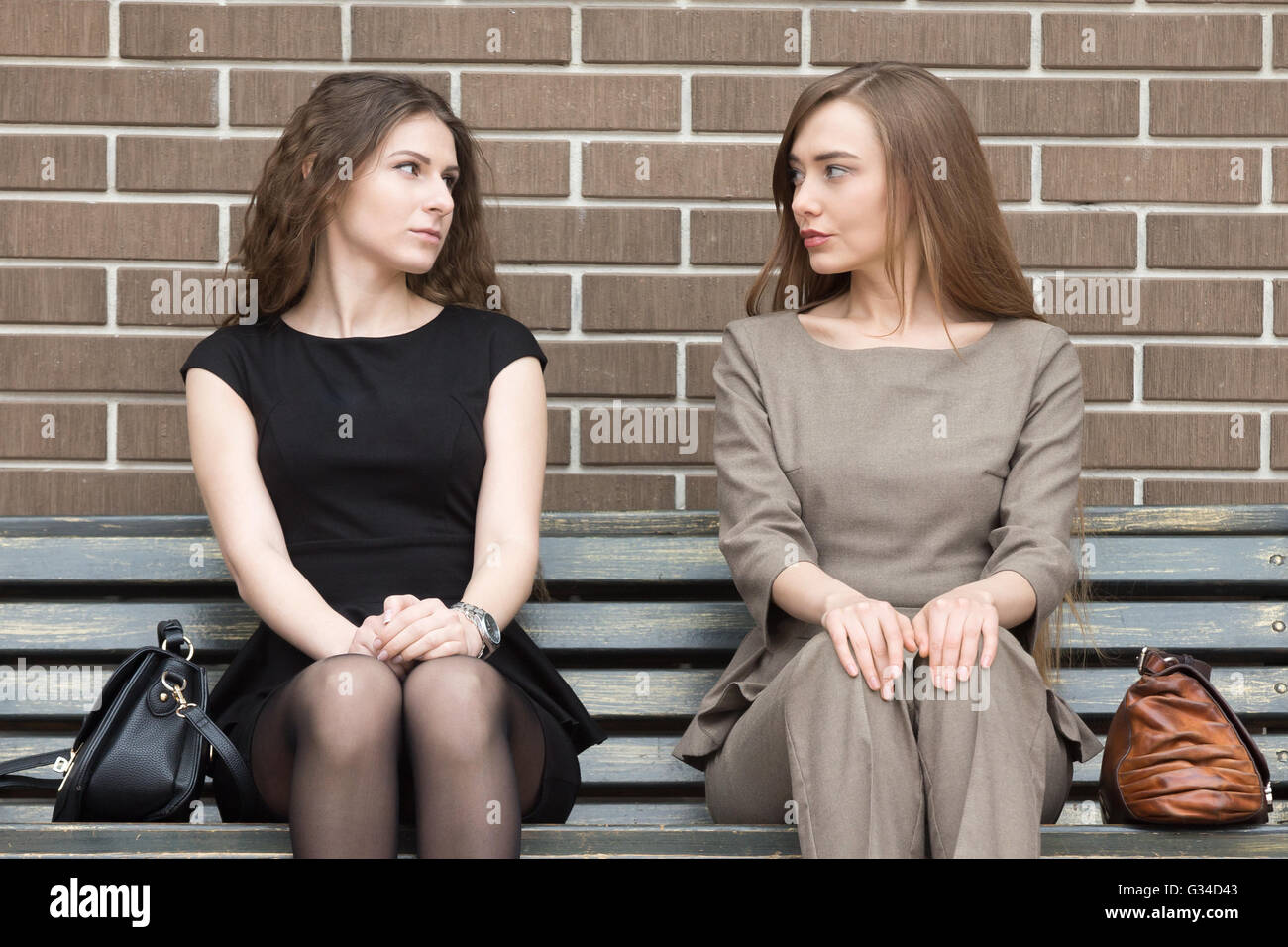 Portrait de deux belles jeunes femmes rivaux assis côte à côte sur le banc et se regardant avec défi Banque D'Images