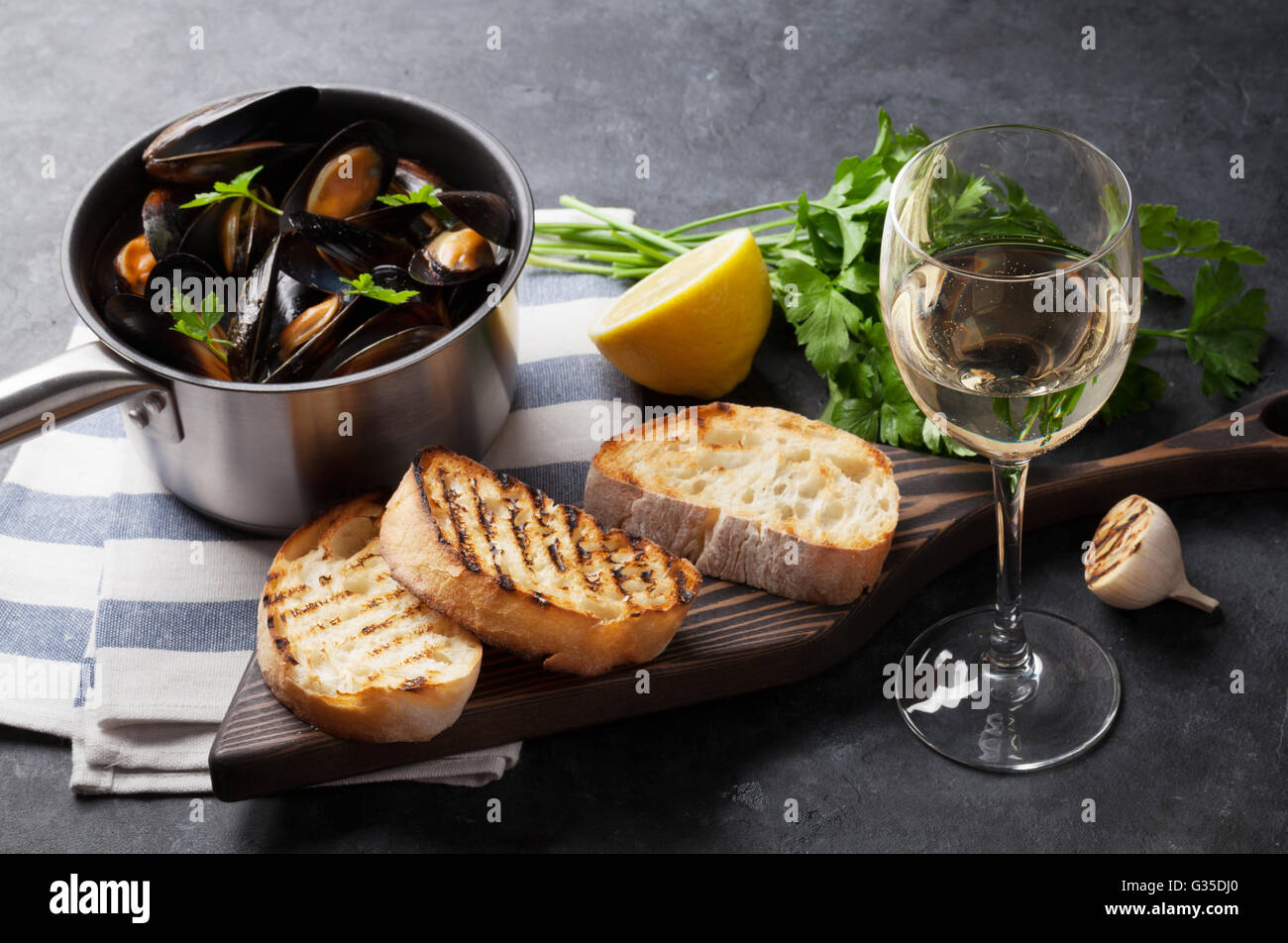 Moules dans marmite en cuivre, toasts de pain et vin blanc sur la table en pierre. Se concentrer sur le verre de vin Banque D'Images