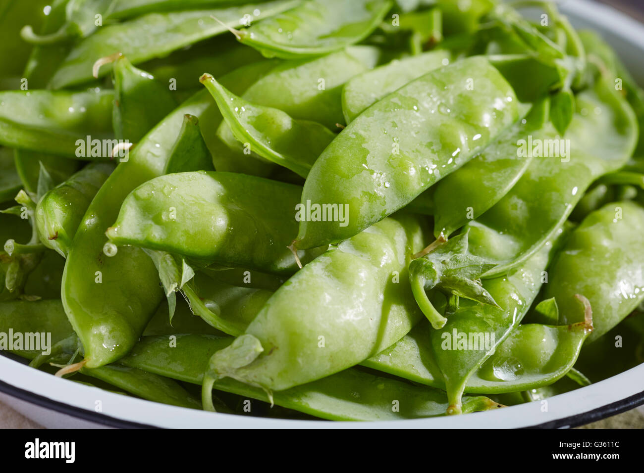 Un bol de matières premières, frais, sucre-snap pois dans leurs gousses Banque D'Images