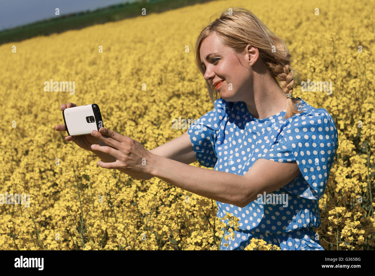 Photo horizontale d'une jeune femme blonde tenant un canola jaune selfies dans un champ de fleurs Banque D'Images
