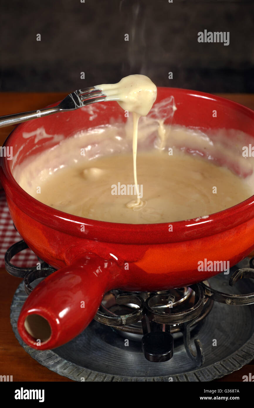 Photo de pain trempé dans le fromage fondu dans le bol à fondue. Banque D'Images