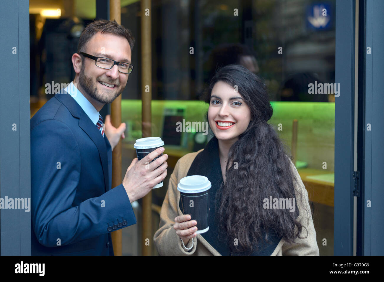 Deux collègues d'acheter du café à emporter laissant un café ou bistro avec les tasses jetables dans leurs mains comme t Banque D'Images