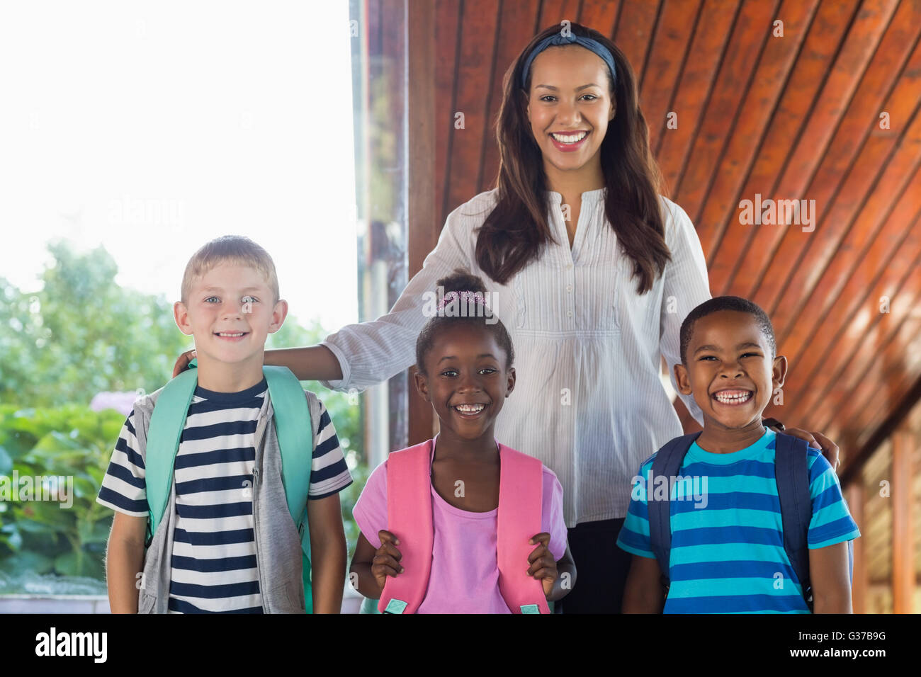 Portrait of smiling teacher et enfants se tenant ensemble avec bras autour de Banque D'Images