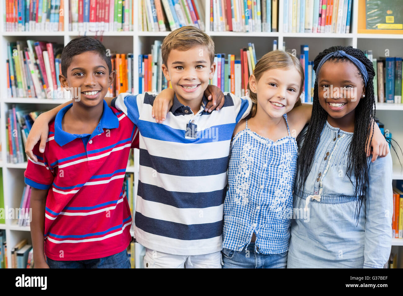 Les enfants de l'école souriant debout avec bras autour de in library Banque D'Images