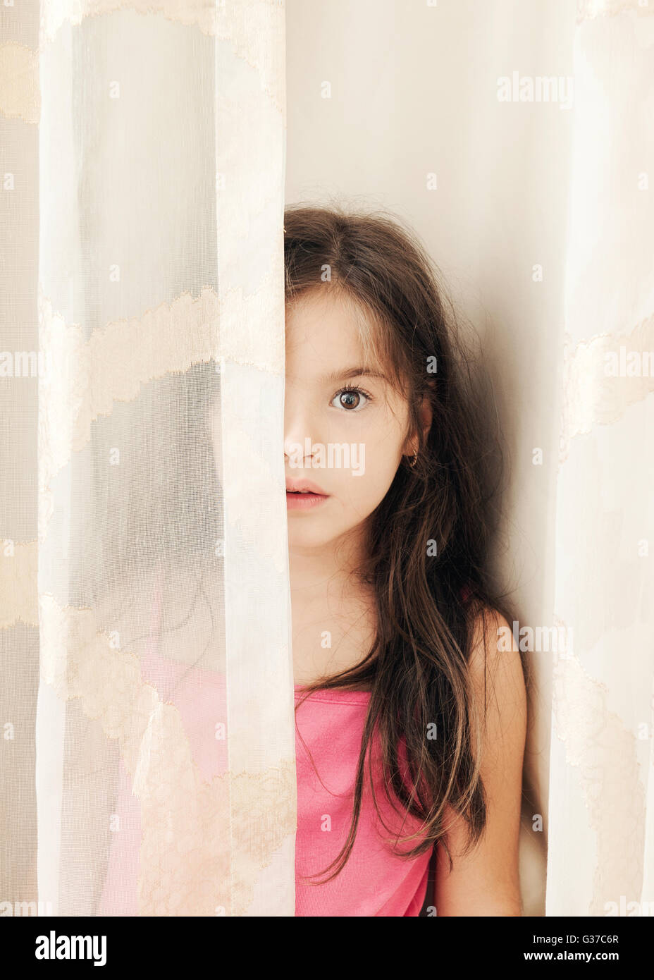 Petite fille se cache derrière un rideau,looking at camera Banque D'Images
