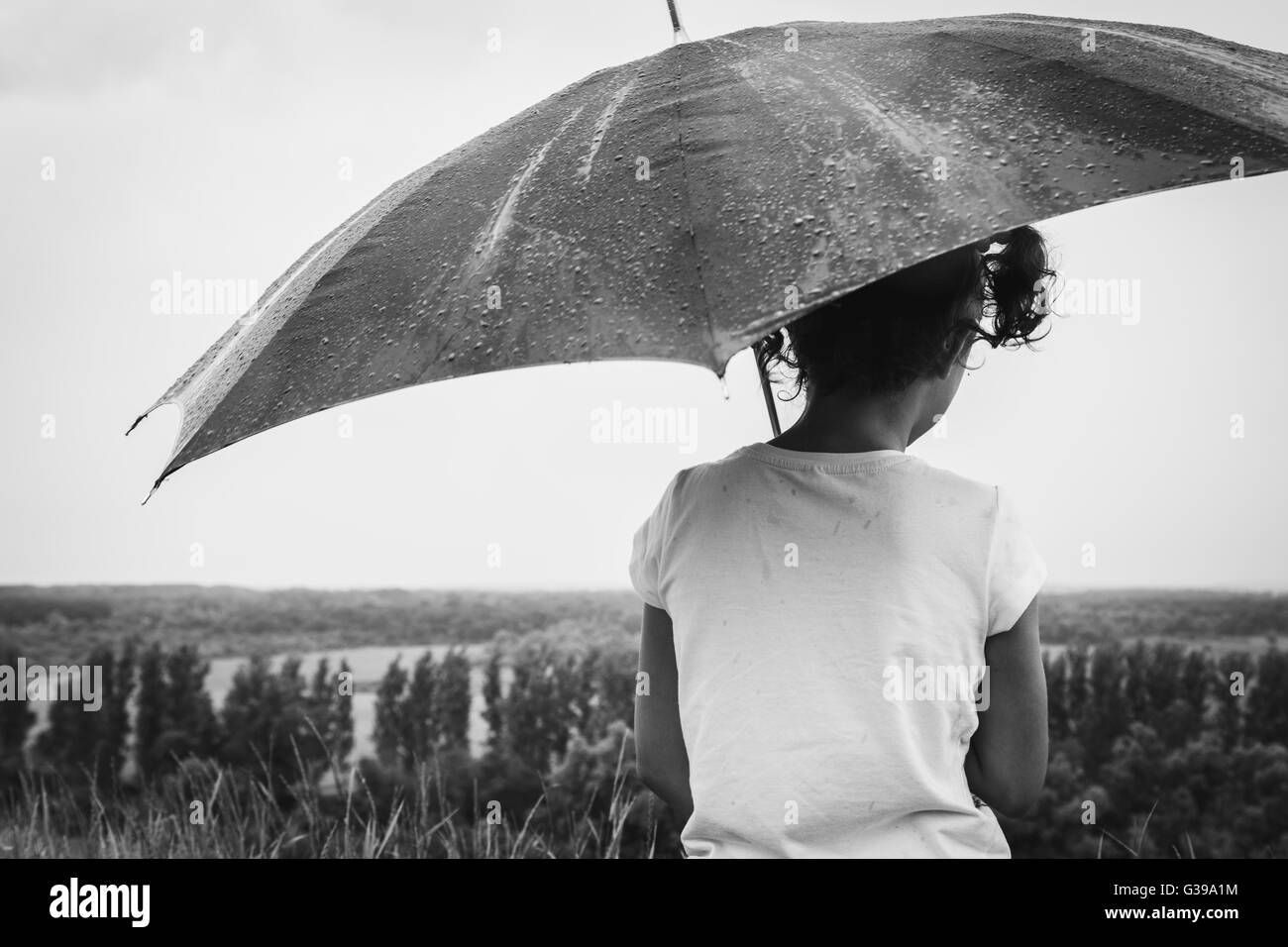 Fille assise sous la pluie avec un parapluie Banque D'Images