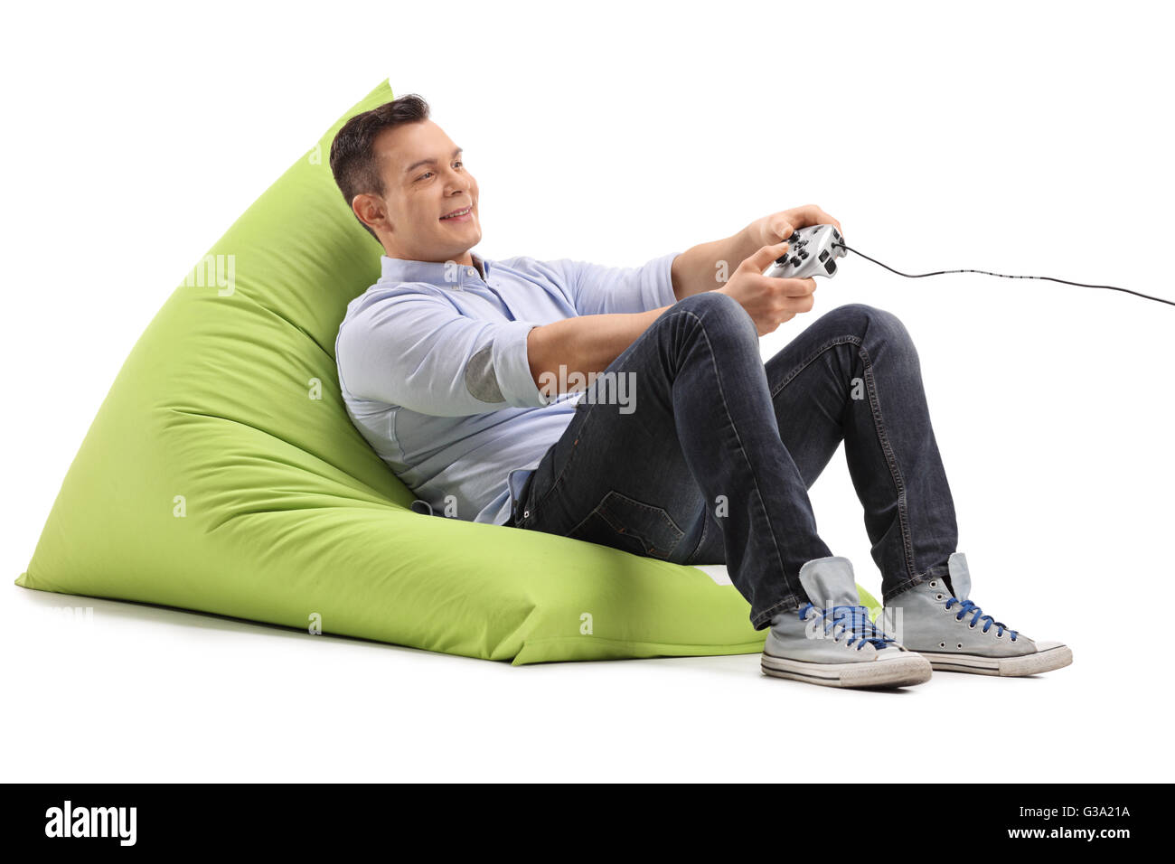 Jeune homme joyeux de jeux vidéo, assis sur un pouf vert isolé sur fond blanc Banque D'Images