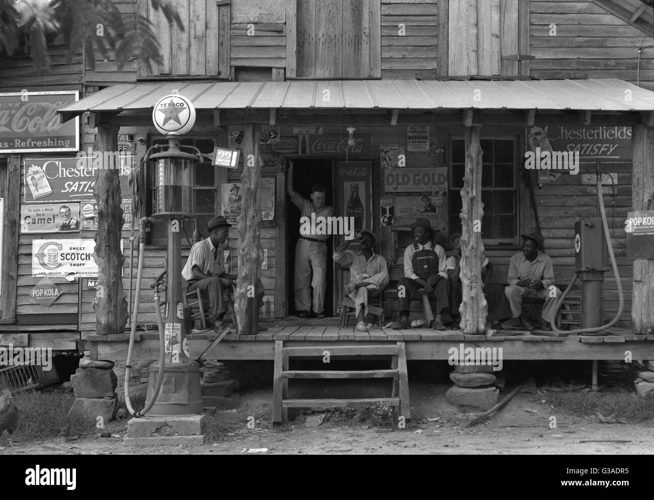 Country store sur chemin de terre. Dimanche après-midi. Remarque la pompe à pétrole sur le droit et la pompe à essence sur la gauche. Bois non fini rugueux, des postes ont été utilisés comme des supports de toit porche. Negro hommes sont assis sur le porche. Le propriétaire du magasin de frère stan Banque D'Images