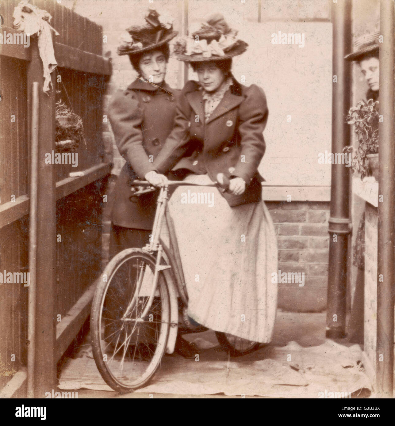 Une jeune femme en plein air "pratiques" de robe jupe sur mesure &AMP ; veste est titulaire d'un vélo stable pour son ami qui est assis sur elle d'avoir sa photo prise. Les deux porter des chapeaux de paille. Date : 1890 Banque D'Images