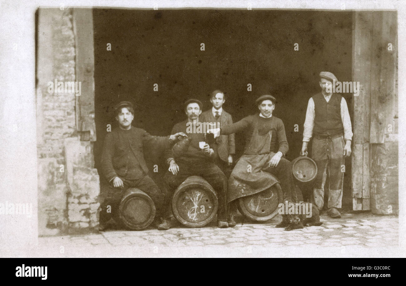 Groupe d'hommes au travail assis sur des tonneaux, avec un chien, France. Date : vers 1920 Banque D'Images