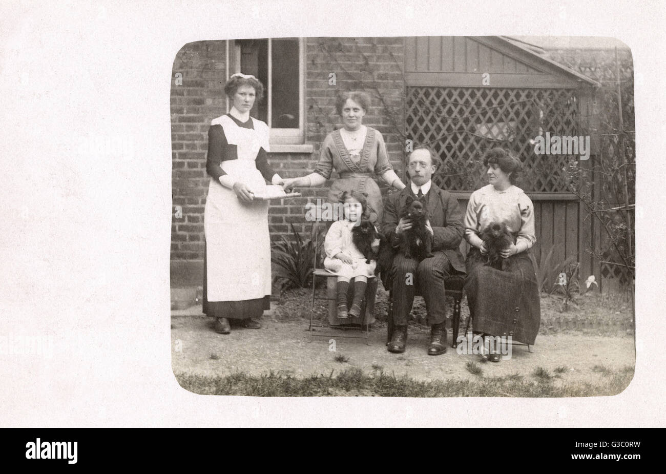 Famille de quatre personnes dans un jardin arrière avec trois lapdogs et un serviteur. Date : vers 1910 Banque D'Images