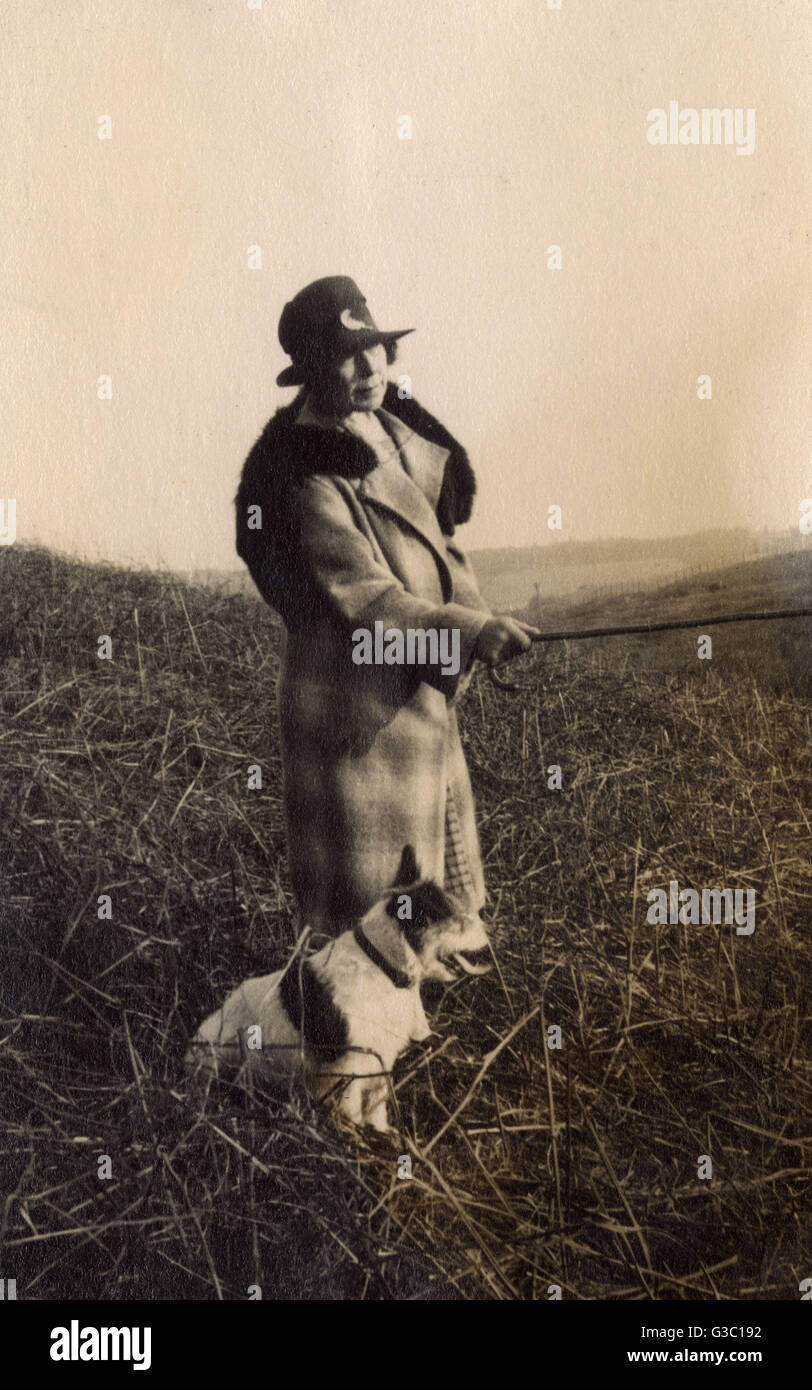 Femme sur la marche avec un chien terrier, pointant quelque chose avec son bâton de marche. Date : vers 1930 Banque D'Images