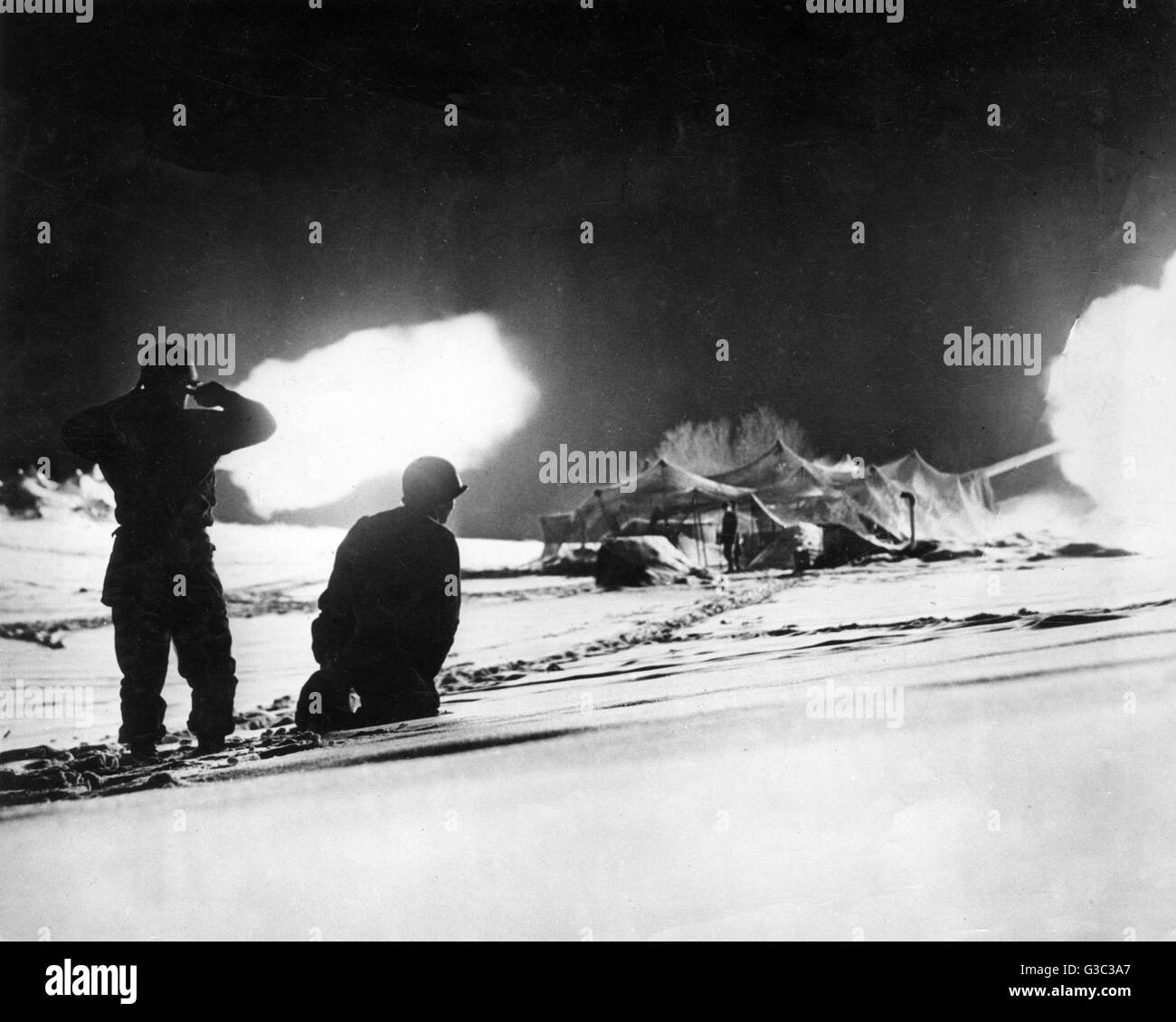 Deux soldats américains sont silhouetté contre le ciel de nuit qui est allumé avec un barrage d'artillerie pendant la Bataille des Ardennes Date : 1944-1945 Banque D'Images