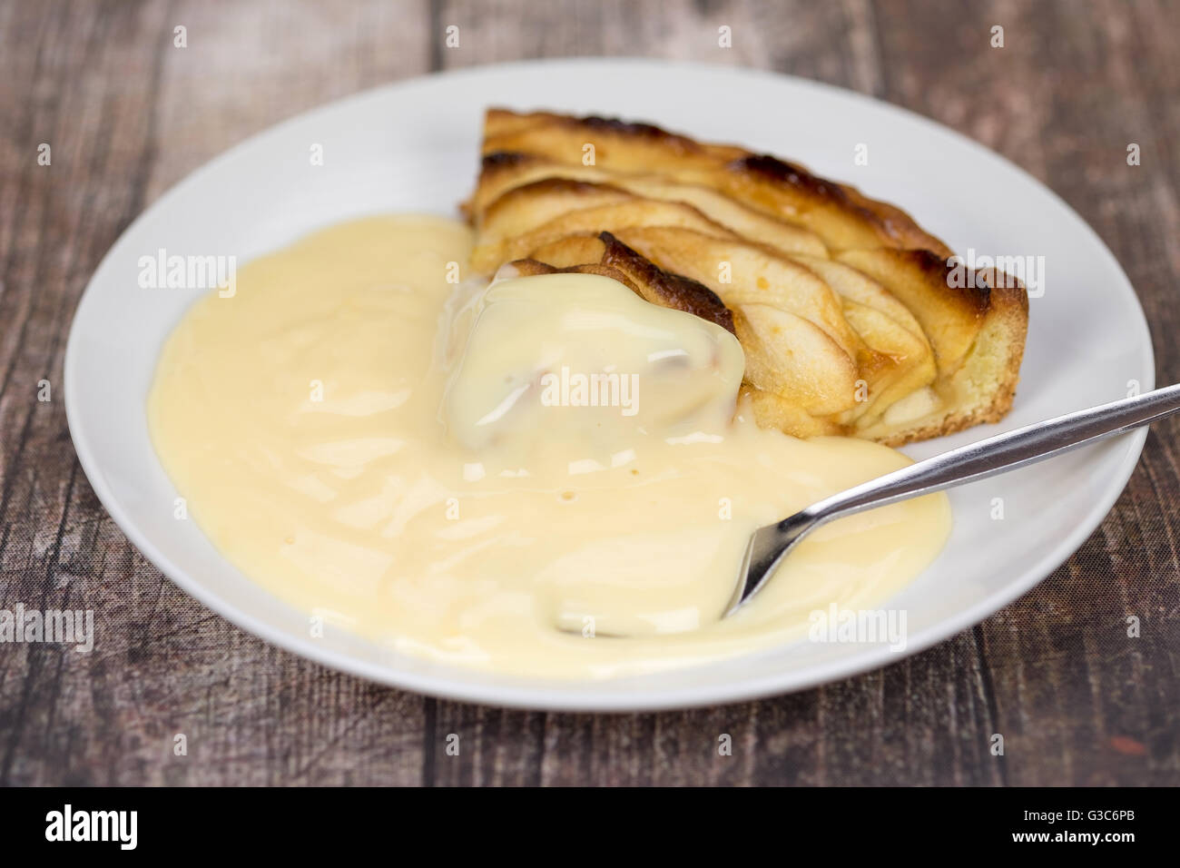 Une tranche de tarte aux pommes et crème anglaise avec une cuillère Banque D'Images