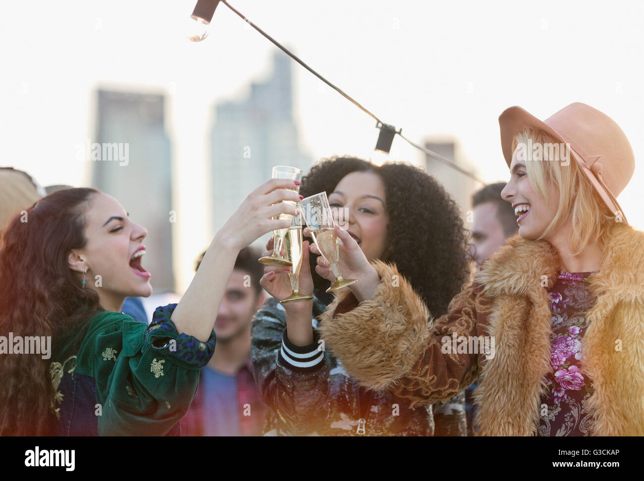 Les jeunes femmes enthousiastes toasting champagne glasses at rooftop party Banque D'Images