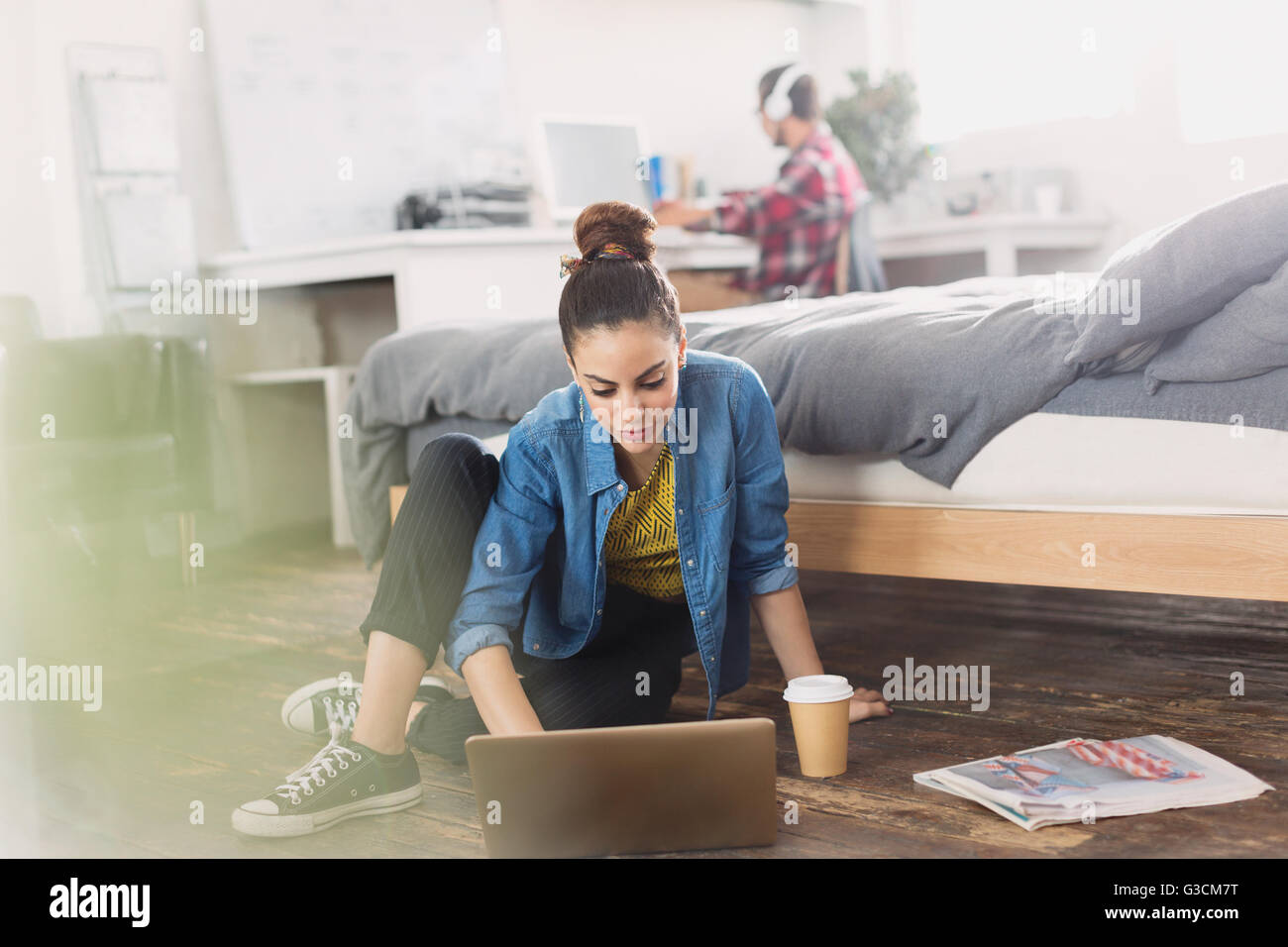 Female college student avec du café à l'aide de l'ordinateur portable sur plancher de chambre à coucher Banque D'Images