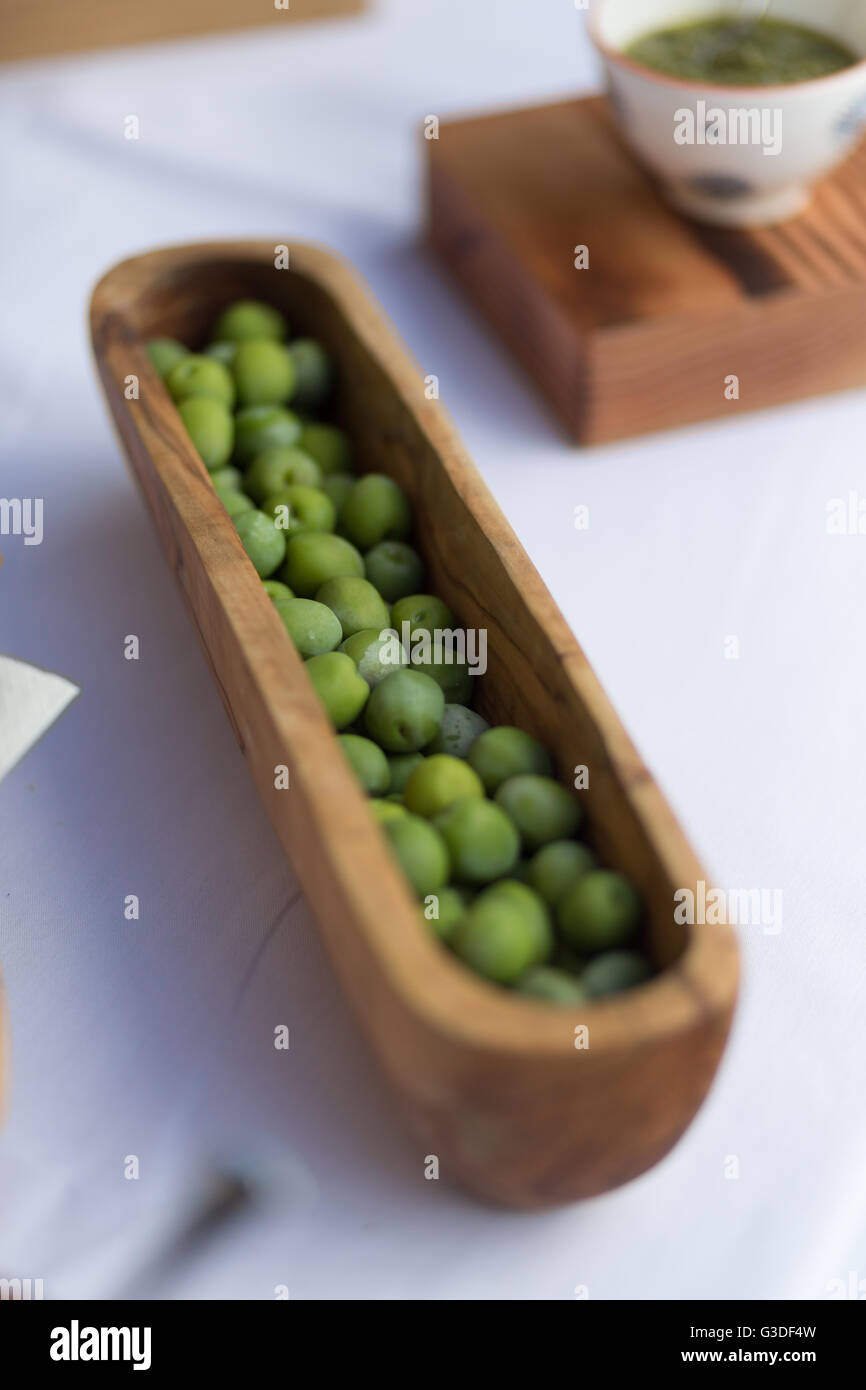 Olives vertes dans un bol en bois sur une nappe blanche Banque D'Images