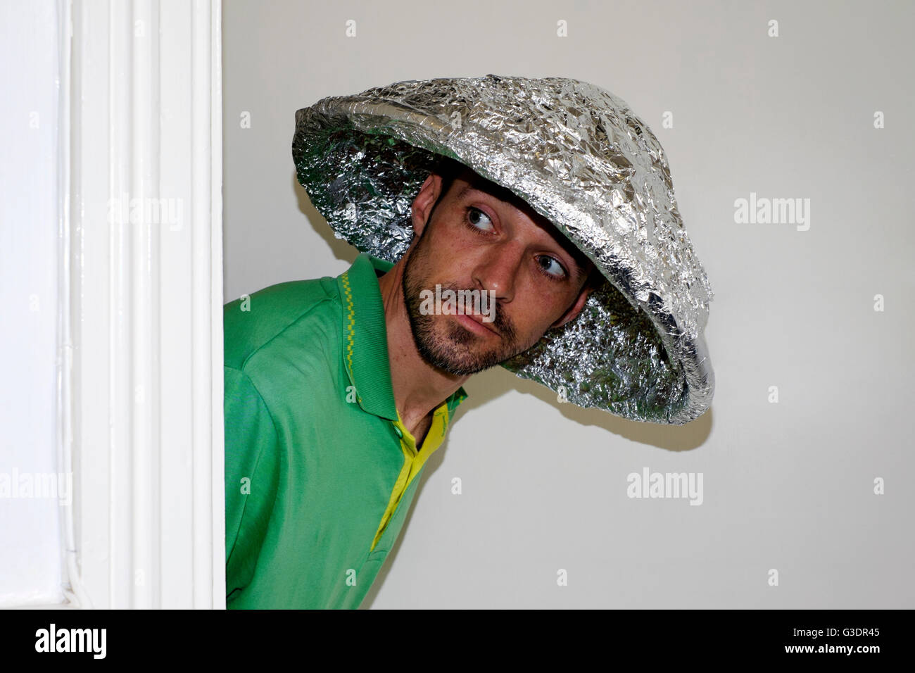 Théorie du complot mâle croyant vêtu d'aluminium hat scrutant de porte Banque D'Images