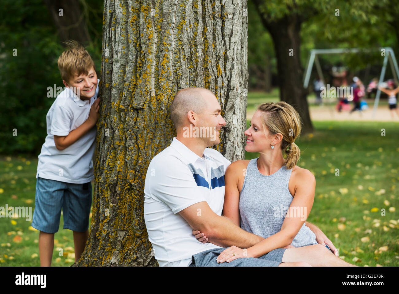 Un couple marié passer du temps de qualité ensemble dans un parc au cours d'une sortie en famille avec leur fils d'oeil de derrière un arbre ; Edmonton, Alberta, Canada Banque D'Images