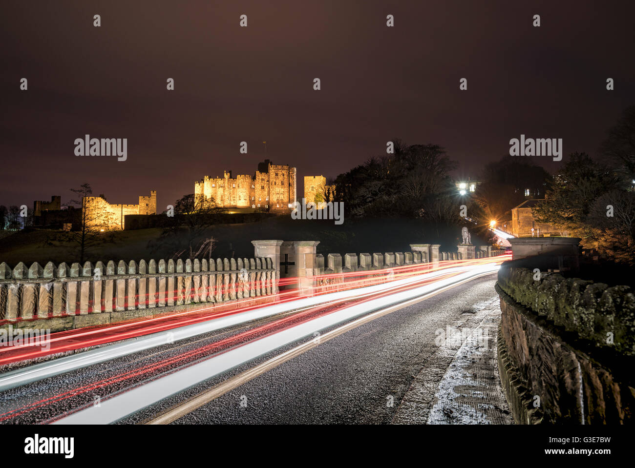 Des sentiers de lumière sur une route et bâtiment en arrière-plan éclairé à la nuit ; Alnwick, Northumberland, Angleterre Banque D'Images