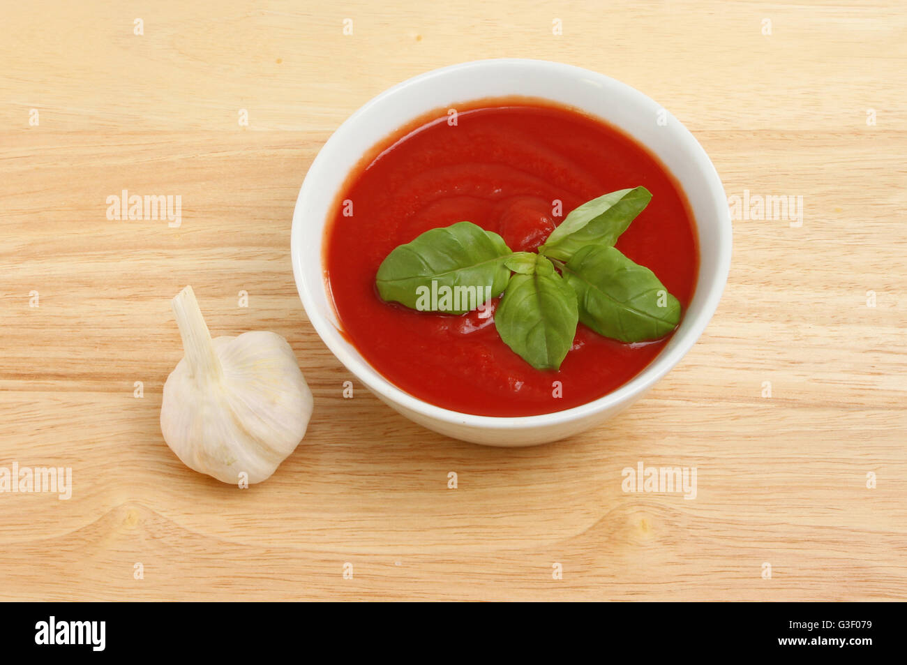 Purée de tomate et le basilic dans un bol avec un bulbe d'ail sur une planche à découper en bois Banque D'Images