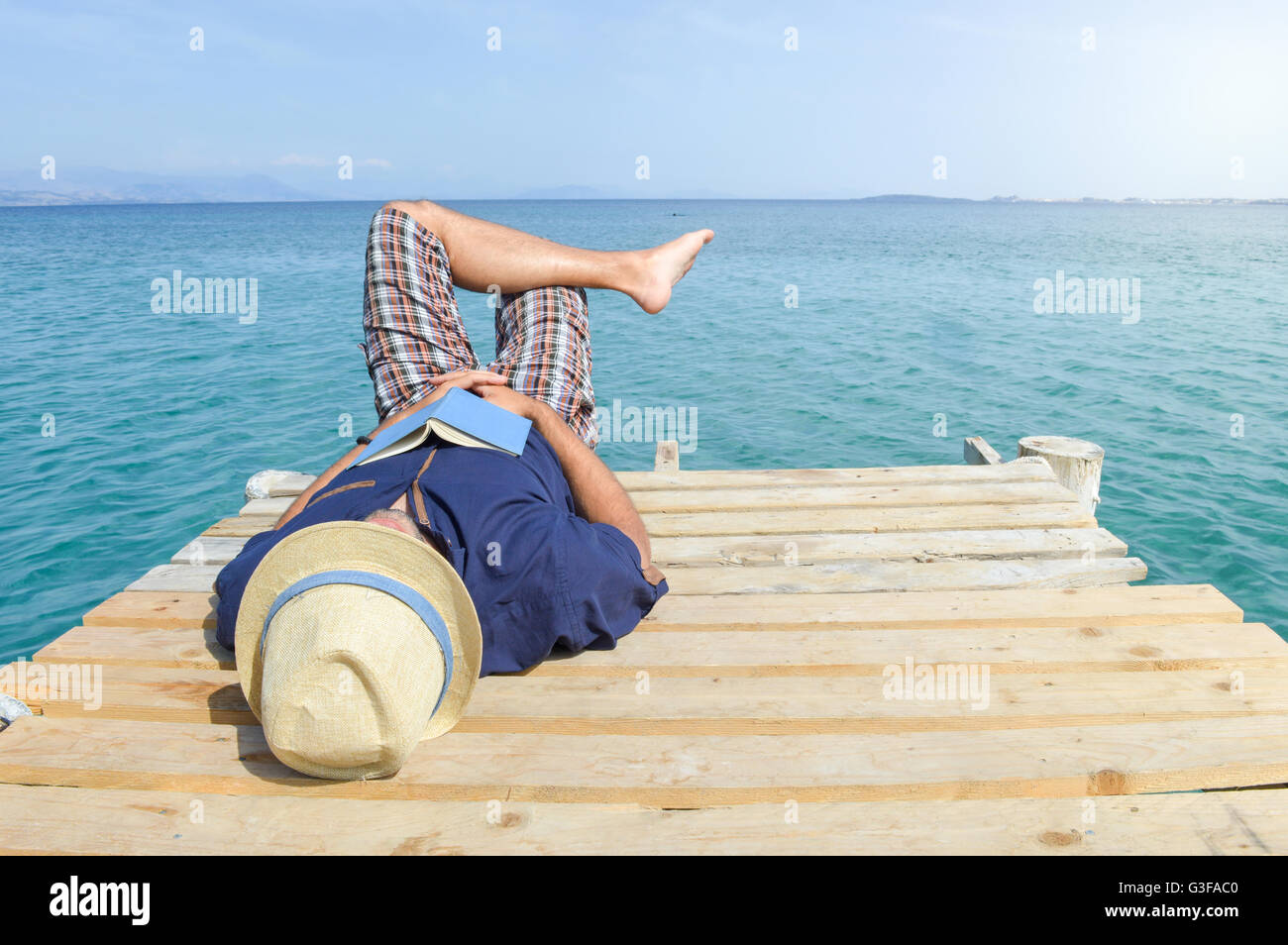L'homme allongé sur le dock avec un livre. Vacances d'Été Espace détente Banque D'Images
