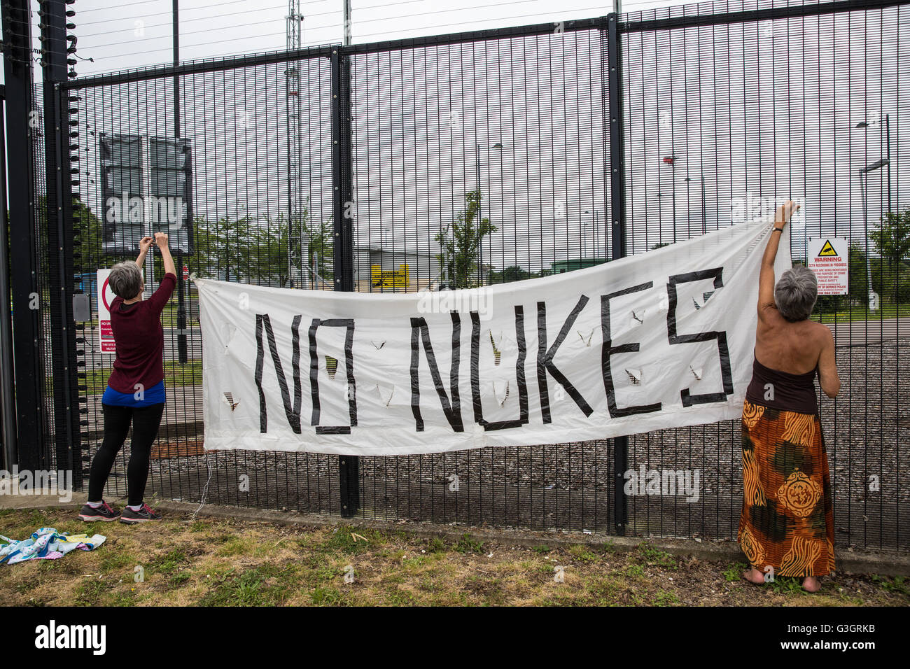 Burghfield, UK. 11 Juin, 2016. Ex-Greenham les militants de la paix commune accrocher un 'No nukes' bannière sur la clôture périphérique de l'AWE Burghfield sur la cinquième journée consécutive d'un blocus de l'entrée des livraisons dans le cadre d'un mois d'action contre le renouvellement du Trident destiné "aux blocus, à occuper et à perturber l'usine" responsable de l'assemblage final de Trident monté des têtes nucléaires. Credit : Mark Kerrison/Alamy Live News Banque D'Images