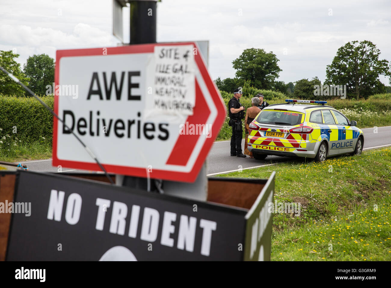 Burghfield, UK. 11 Juin, 2016. Ministère de la Défense policiers débat avec un militant de la paix s'accrochant des banderoles de la clôture périphérique de l'AWE Burghfield statuts violations au cours d'un blocus de l'entrée des livraisons sur le site. Credit : Mark Kerrison/Alamy Live News Banque D'Images