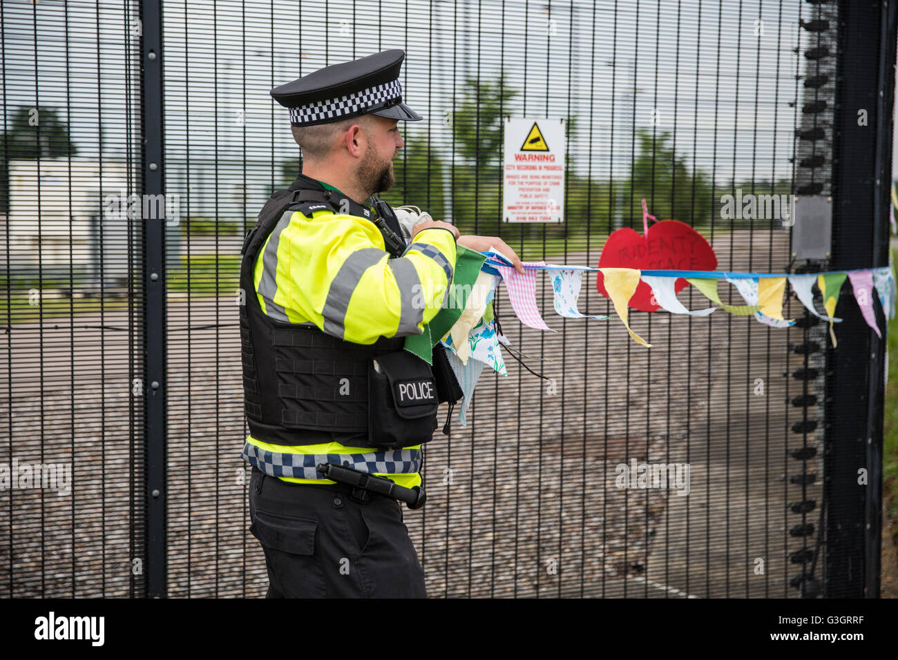 Burghfield, UK. 11 Juin, 2016. Un Ministère de la Défense policier supprime une bannière accrochée par ex-Greenham Common militants de la paix à partir de la clôture périphérique de l'AWE Burghfield en violation alléguée d'un byelaw interdisant de dégradation de la clôture. C'était le cinquième jour consécutif de blocus de l'entrée des livraisons dans le cadre d'un mois d'action contre le renouvellement du Trident à l'extérieur de l'usine responsable de l'assemblage final de Trident monté des têtes nucléaires. Credit : Mark Kerrison/Alamy Live News Banque D'Images