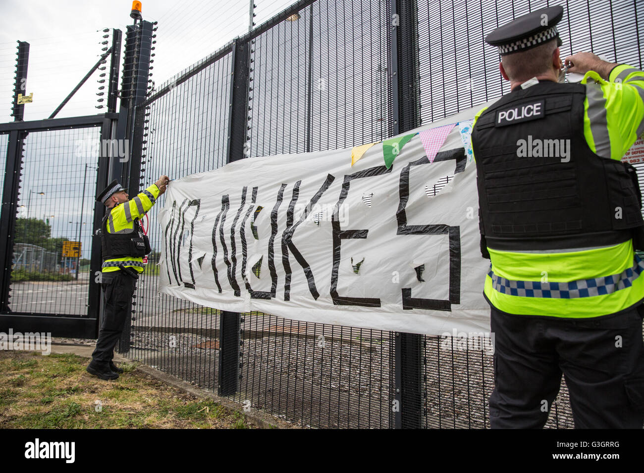 Burghfield, UK. 11 Juin, 2016. Ministère de la Défense policiers enlever une bannière accrochée par ex-Greenham Common militants de la paix à partir de la clôture périphérique de l'AWE Burghfield en violation alléguée d'un byelaw interdisant de dégradation de la clôture. C'était le cinquième jour consécutif de blocus de l'entrée des livraisons dans le cadre d'un mois d'action contre le renouvellement du Trident à l'extérieur de l'usine responsable de l'assemblage final de Trident monté des têtes nucléaires. Credit : Mark Kerrison/Alamy Live News Banque D'Images