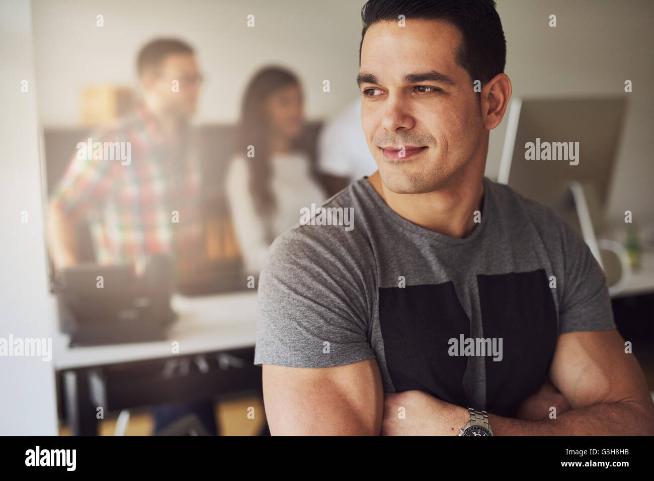 Close up de calme beau mâle travailleur avec bras musclé plié portant chemise à manches courtes gris en petit bureau avec d'autres em Banque D'Images