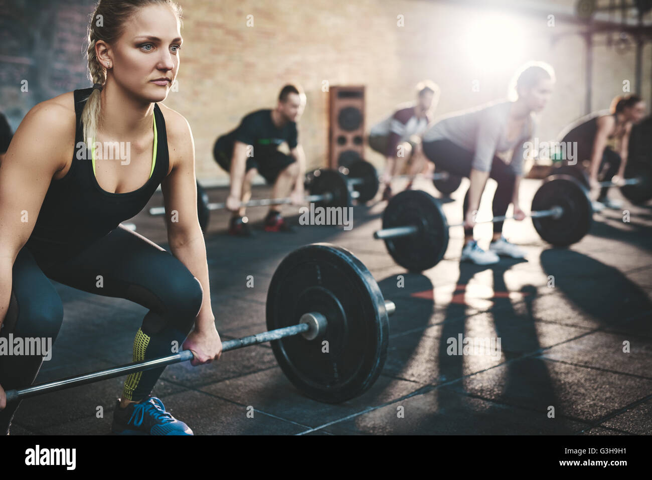 Fit young woman lifting des barres à l'accent, s'entraîner dans un gymnase avec d'autres personnes Banque D'Images