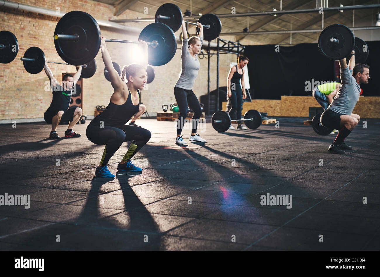Mettre en place les jeunes tiges de levage au-dessus de leurs têtes à l'accent, s'entraîner dans un gymnase avec d'autres personnes Banque D'Images