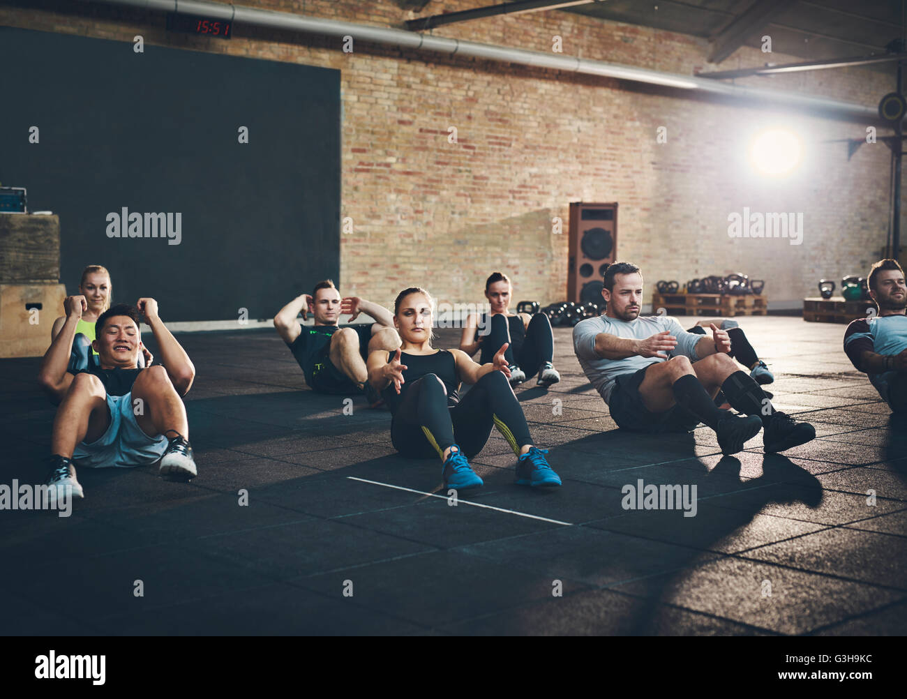 Groupe d'adultes d'athlétisme les hommes et les femmes exécutant s'asseoir des exercices pour renforcer leurs muscles abdominaux de base à la formation de remise en forme Banque D'Images