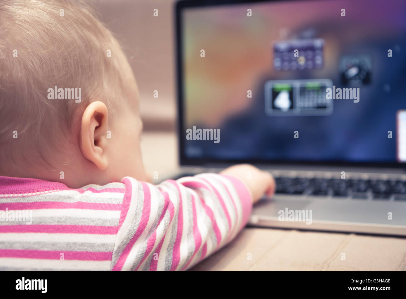 Bébé à travailler sur un ordinateur portable. Vue de derrière le bébé avec la main d'atteindre à l'ordinateur Banque D'Images