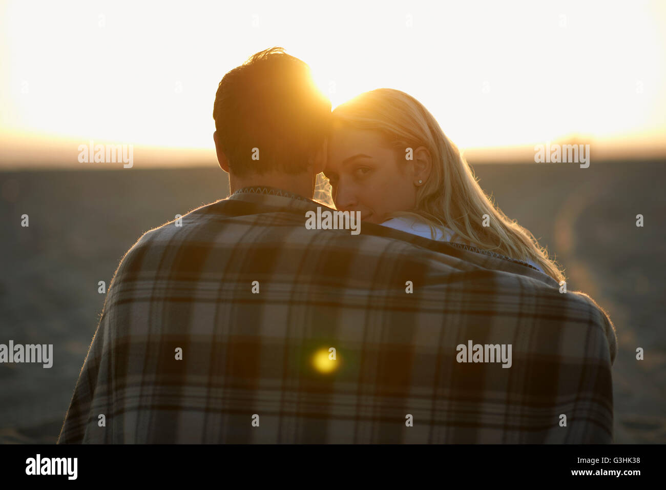 Couple on beach, au coucher du soleil, enveloppé dans une couverture, young woman looking over shoulder Banque D'Images
