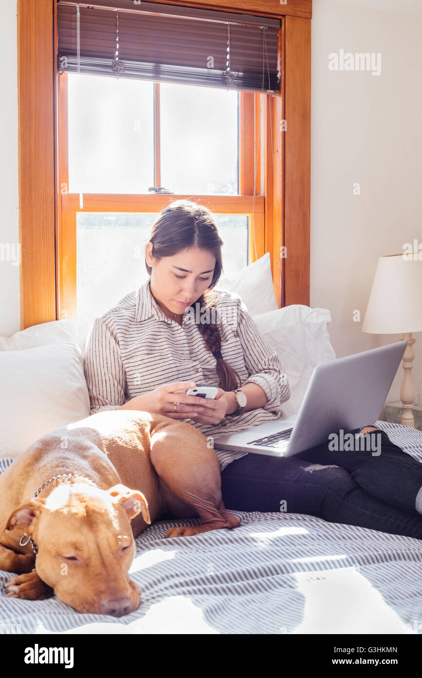 Femme assise sur le lit avec chien et coffre using smartphone Banque D'Images