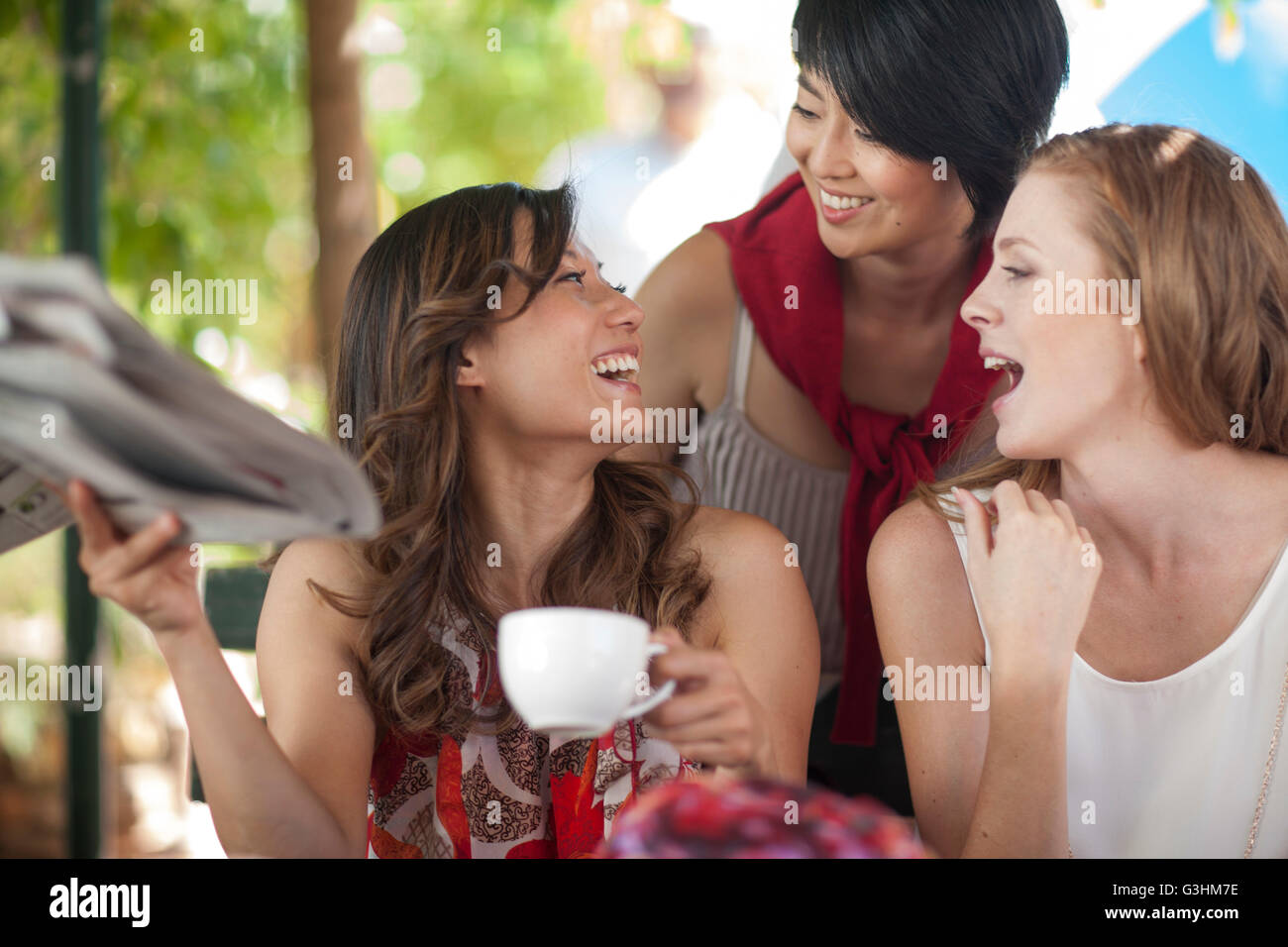 Trois amies laughing at sidewalk cafe in city Banque D'Images