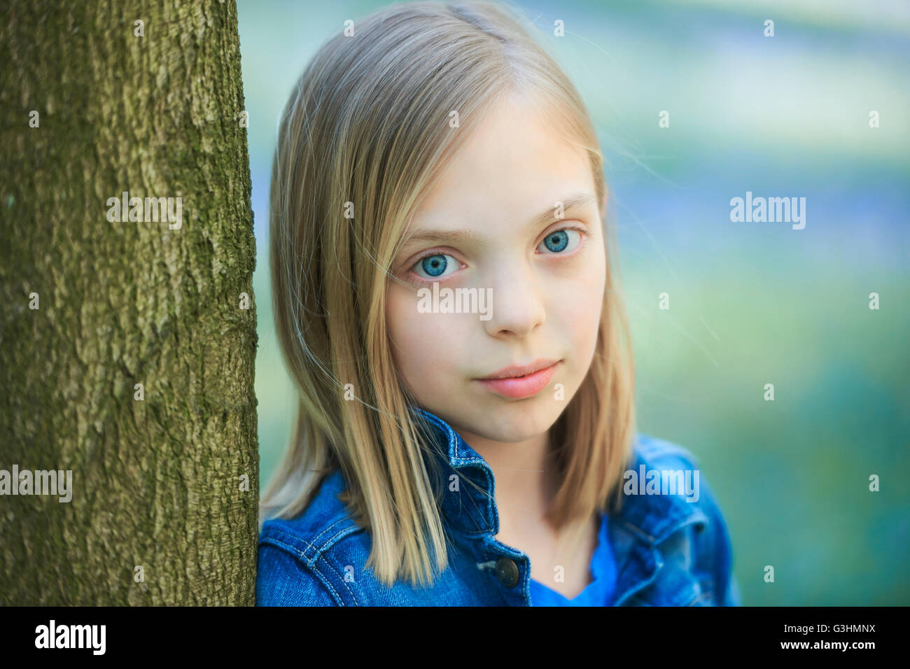 Portrait de jeune fille blonde appuyée contre arbre en forêt, bluebell Hallerbos, Bruxelles, Belgique Banque D'Images