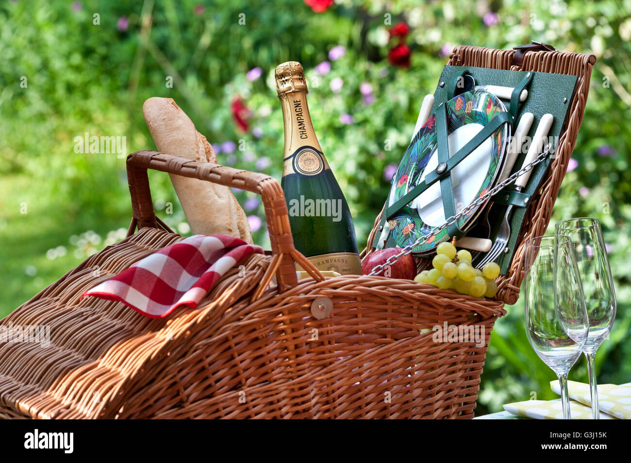 Pique-nique bouteille de champagne française baguette raisin et panier pique-nique en osier dans un jardin fleuri luxueux et ensoleillé en plein air Banque D'Images