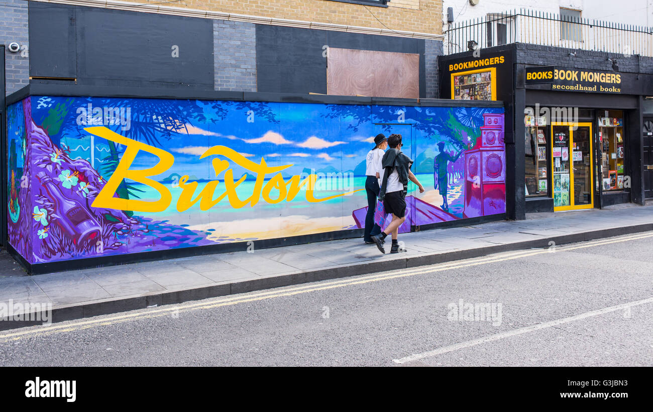 Hipster couple en train de marcher en face de graffiti murale avec le mot Brixton écrit sur un arrière-plan avec tropical beach et cocktail Banque D'Images