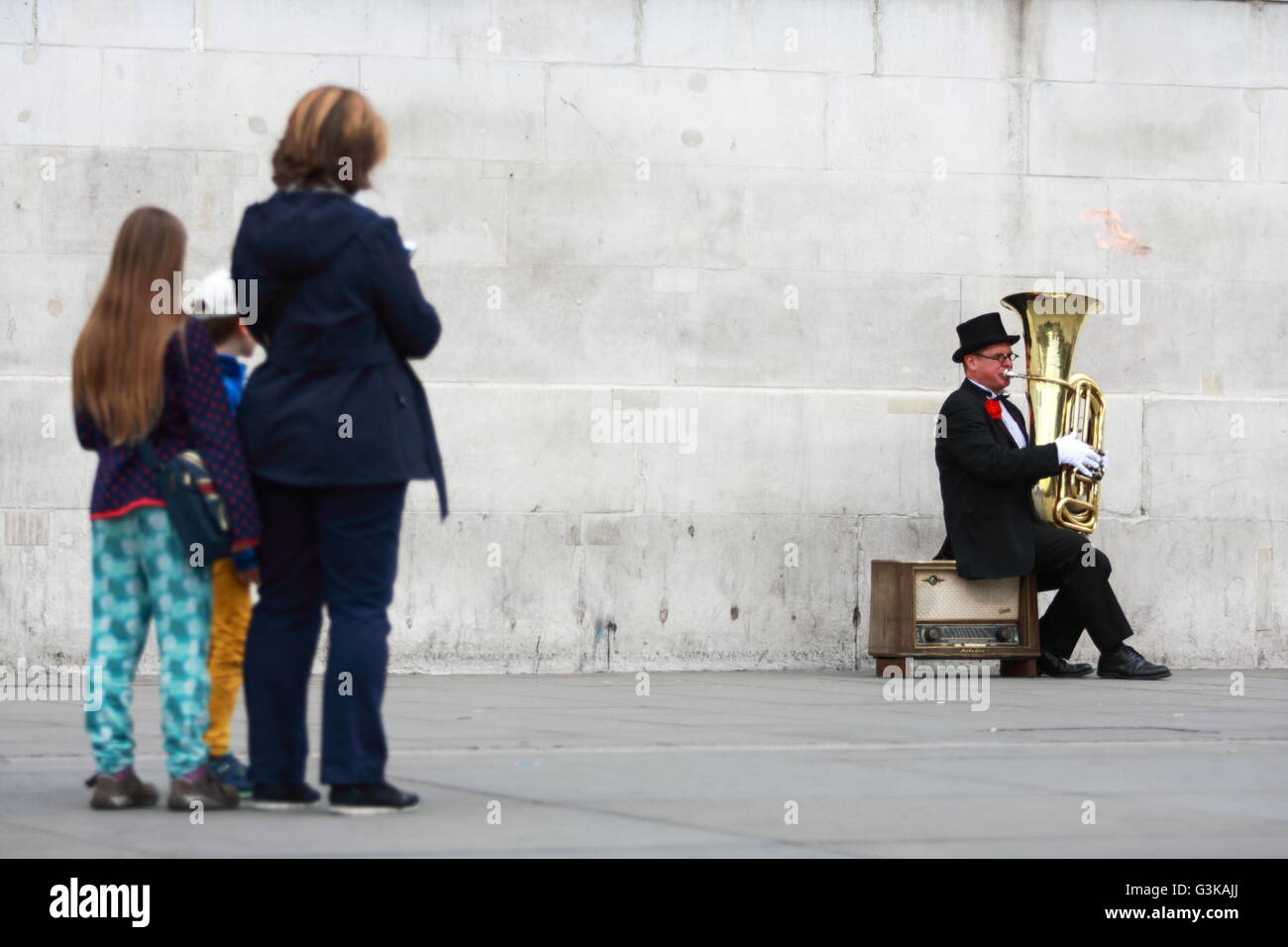 Un artiste de rue joue un tuba à Trafalgar Square, Londres, vu par une femme et deux enfants. Banque D'Images