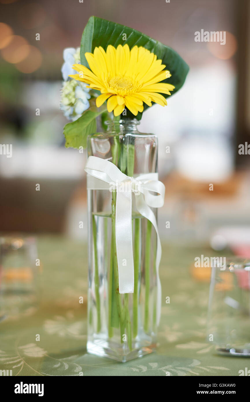 Un petit verre vase de fleurs jaune vert sur une table à la réception de mariage. Banque D'Images