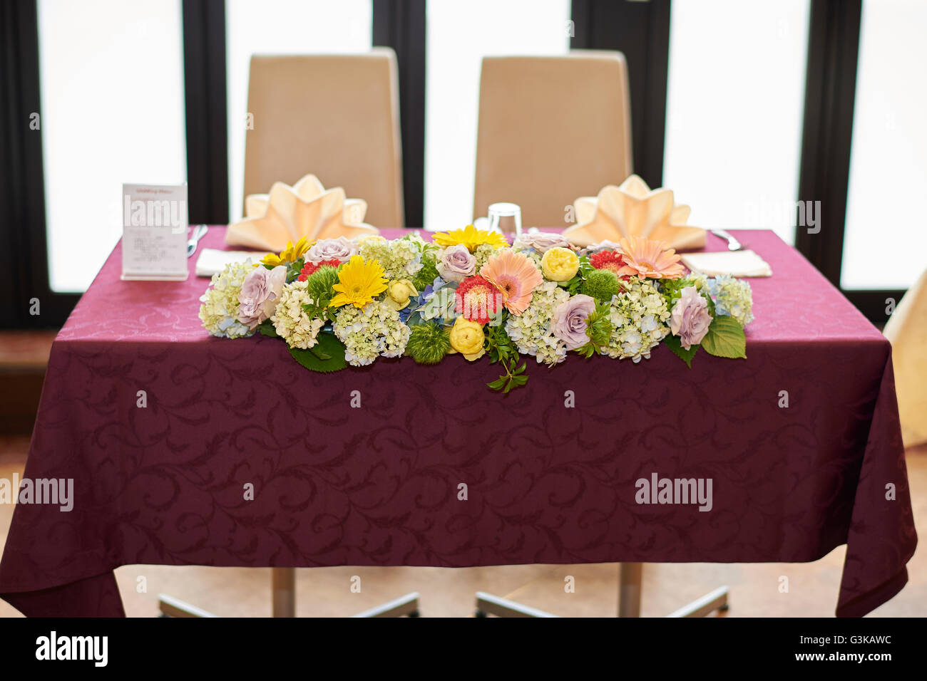 Un gros bouquet de fleurs assorties sur la table d'honneur à une réception de mariage avec un chiffon de table rouge et de grandes fenêtres derrière elle. Banque D'Images